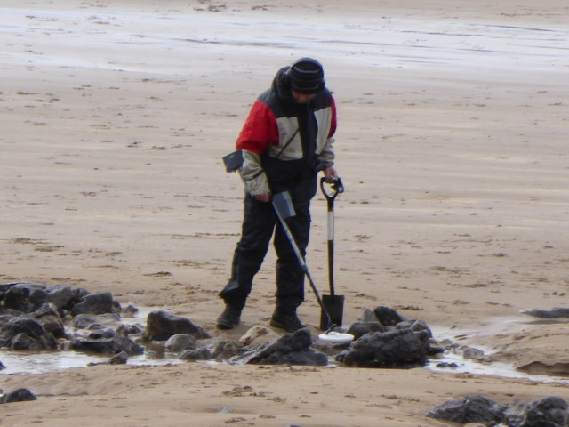 A detectorist with a metal detector and spade on the beach at Langland Bay, Gower